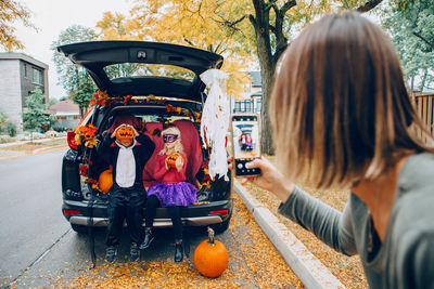 Mother taking pictures of kids sitting in car trunk