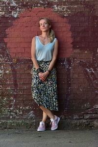 Full length portrait of woman standing against brick wall