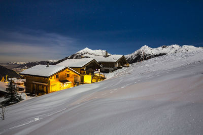 Chalets at snow covered mountain against blue sky at night during winter