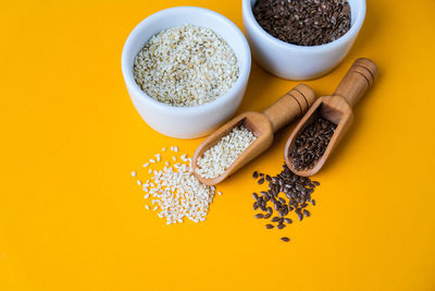 Wooden spoons with sesame and flax seeds lies in a white mortar on a yellow background. healthy eat