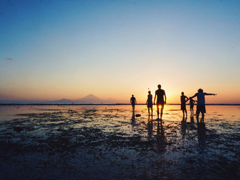 People enjoying on beach against sky during sunset