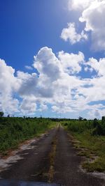 Empty road amidst field against sky