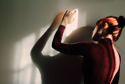 Rear view of woman standing against wall at home