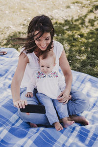 Smiling mother taking selfie with cute daughter while sitting on blanket in park