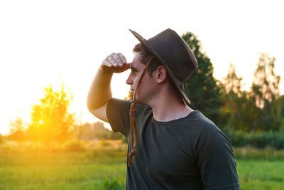 Young man farmer in cowboy hat at agricultural field on sunset with sun flare. closeup portrait 