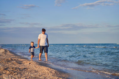 Full length of man and son on beach against sky