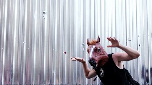 Portrait of man wearing horse mask against metal fence