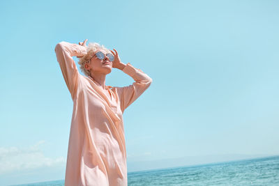 Rear view of woman with arms raised standing at beach against clear blue sky