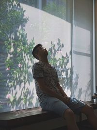 Side view of woman sitting on window at home