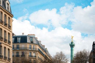 Low angle view of july column and buildings in city against cloudy sky