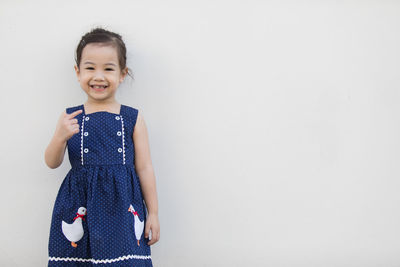 Portrait of a smiling girl standing against white wall