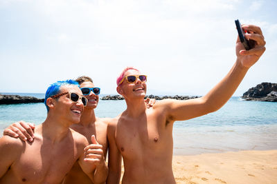 Shirtless boys doing selfie while standing by sea