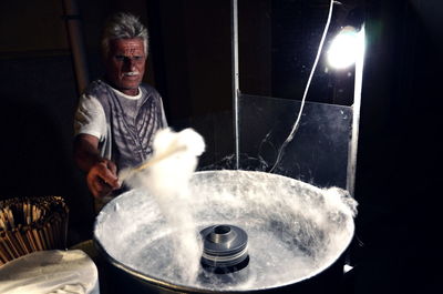 Vendor twirling cotton candy in machine at stall during night