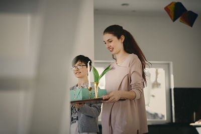 Smiling sister and brother carrying gift with serving tray while walking at home