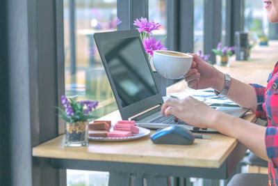 Midsection of businesswoman holding coffee cup by laptop on table at cafe