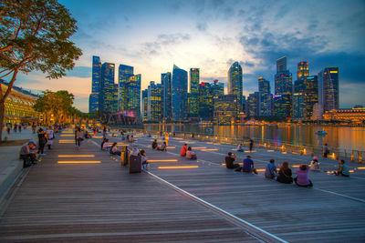 People on promenade by river against sky in city during sunset