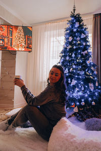 Beautiful young girl sitting next to the christmas tree. new year decoration. home interior. winter
