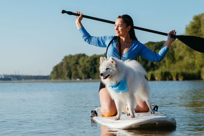 Snow-white japanese spitz dog standing on sup board, woman paddleboarding with her pet on city lake