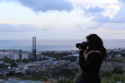 Side view of woman photographing cityscape against sky