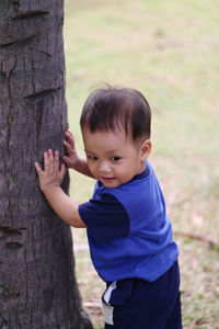 Cute boy standing by tree trunk