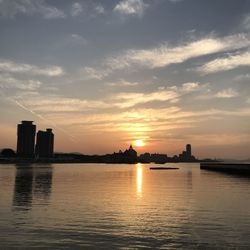 Silhouette buildings by river against sky during sunset