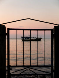 Silhouette gate by sea against sky during sunset