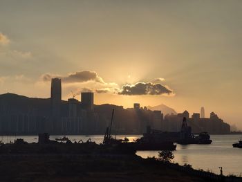 Silhouette buildings by sea against sky during sunset