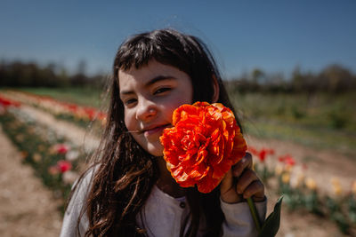 Portrait of girl holding big orange tulip in colorful flower field