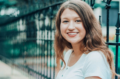 Portrait of smiling teenager standing by railing outdoors