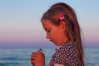 Adorable little girl looks on flower on beach.cute child with wet long hair in dress smelling flower