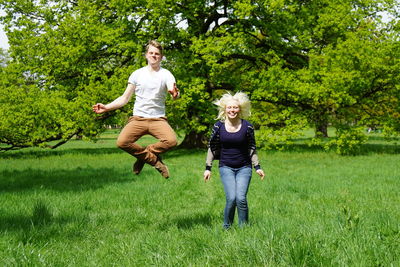 Cheerful couple jumping over grassy field in park
