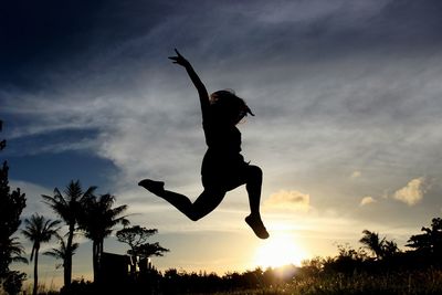 Low angle view of silhouette girl jumping in mid-air against sky at sunset