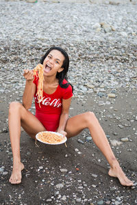 Portrait of smiling young woman eating noodles while sitting at beach