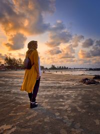 Rear view of woman standing at beach during sunset
