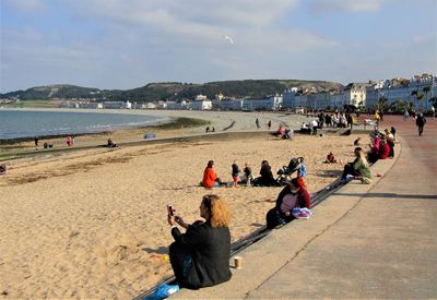 Woman smiling whilst taking a video on her mobile phone at the beach.