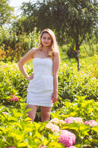 Portrait of smiling young woman standing by flowering plants