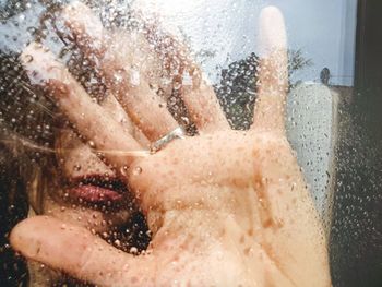 Close-up portrait of woman seen through wet glass window