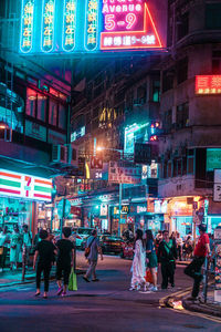 People walking on illuminated street in city at night