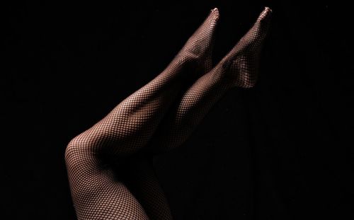 Low section of woman wearing stockings against black background