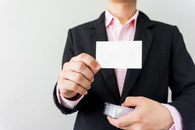 Midsection of man holding paper against white wall