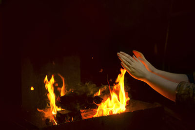 Cropped hand of man burning firewood at night