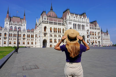 Back view of beautiful girl enjoying view of hungarian parliament building in budapest, hungary