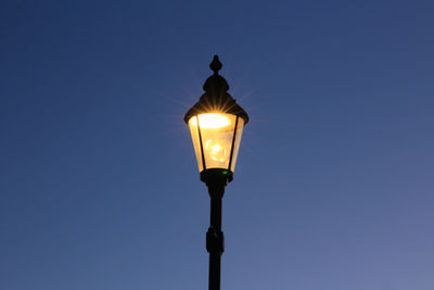 Low angle view of illuminated street light against blue sky