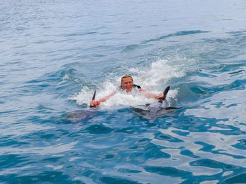 Smiling mid adult woman holding dolphins swimming in sea