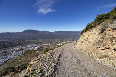 Scenic view of road by mountains against blue sky