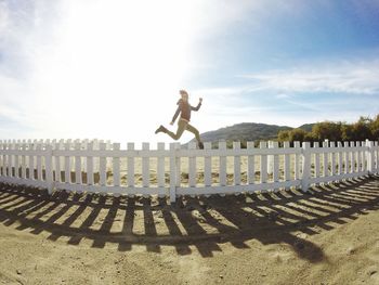 Full length of woman jumping over fence at beach