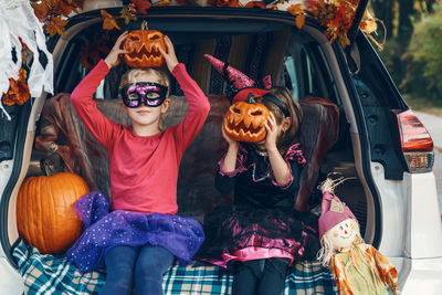 Portrait of cute kids holding pumpkin sitting in car trunk