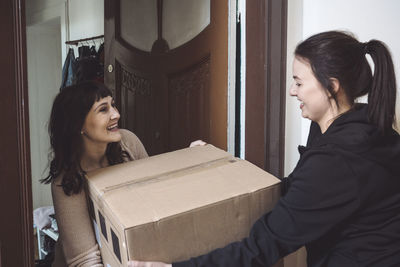 Smiling delivery woman delivering package to customer while talking at doorstep