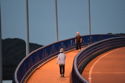 Rear view of woman walking on footbridge against clear sky