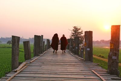 Rear view of women walking on footpath against sky during sunset